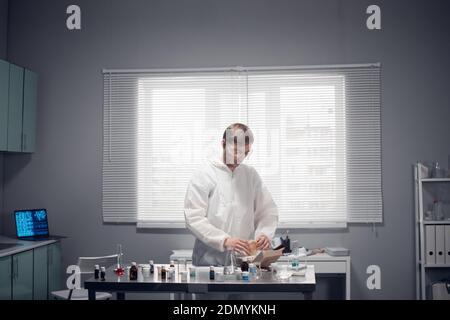 Un jeune ouvrier de laboratoire ayant une pause déjeuner, mangeant un hamburger dans son bureau. Banque D'Images