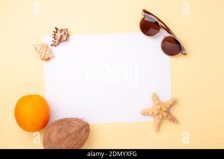 Papier vierge, lunettes de soleil, fruits exotiques, coquillages et étoiles de mer sur fond jaune. Concept de vacances d'été - image Banque D'Images