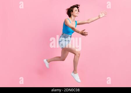 Photo de profil de la taille du corps de joli mignon sportif jeune fille sourire courir saut vers l'ami veulent embrasser le denim mini-jupe bleu sneakers singlet Banque D'Images