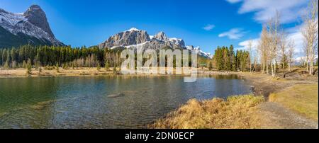 Quarry Lake park lakeshore in late autumn season sunny day morning. Snow capped Mount Rundle and Mount Lawrence Grassi Ha Ling Peak in with blue sky Stock Photo