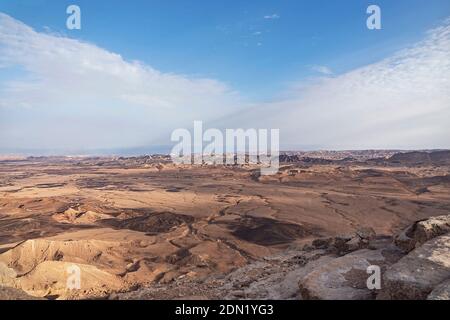 two soft windblown clouds overlap above the maktesh ramon crater in israel with the mountains of jordan in the far background Stock Photo