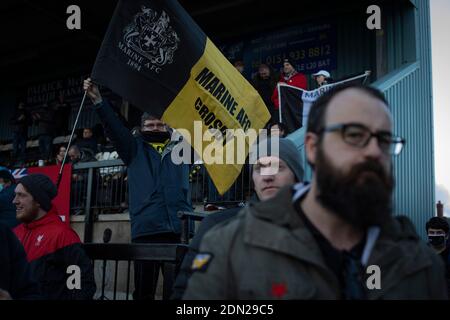 A home supporter with a flag welcomes their team on to the pitch before Marine play Hyde United in an FA Trophy first round tie at the Marine Travel Arena, formerly known as Rossett Park, in Crosby. Due to coronavirus regulations which had suspended league games, the Merseysiders’ only fixtures were in cup competitions, including their forthcoming tie against Tottenham Hotspur in the FA Cup third round. Marine won the game by 1-0, watched by a permitted capacity of 400, with the visitors having two men sent off in the second half. Stock Photo