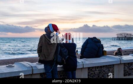 Brighton Royaume-Uni 17 décembre 2020 - UN couple à Santa Hats profiter du coucher de soleil sur le front de mer de Brighton à la fin d'une journée lumineuse sur la côte sud . La ville de Brighton et Hove a été maintenue dans les restrictions de niveau deux de coronavirus en Angleterre après une annonce plus tôt aujourd'hui par le secrétaire à la Santé Matt Hancock : crédit Simon Dack / Alamy Live News Banque D'Images