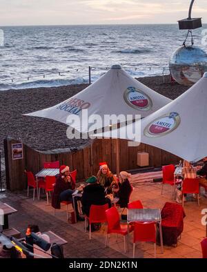 Brighton UK 17th December 2020 - This group dressed in Santa hats enjoy some food and drinks outside at a Brighton seafront bar at the end of a bright day on the South Coast . The city of Brighton and Hove has been kept in coronavirus Tier Two restrictions in England after an announcement  earlier today by the Health Secretary Matt Hancock : Credit Simon Dack / Alamy Live News Stock Photo