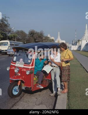 Thaïlande. Bangkok. Touristes parlant avec le chauffeur de taxi tuk-tuk au bord de la route. Banque D'Images