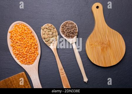 assortiment de lentilles se mélangent avec des lentilles rouges, brunes et noires dans des cuillères en bois sur fond noir une dame plate avec vue de dessus. Banque D'Images