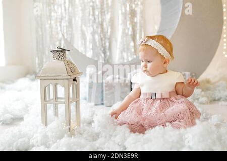 Petite fille en robe rose, qui ressemble à un petit ange, assise en laine de coton artificielle près de lanterne blanche dans l'intérieur du studio Banque D'Images