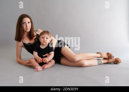 Jeune belle mère en petite robe noire couchée avec elle fils sur le sol et prendre un foto en studio Banque D'Images