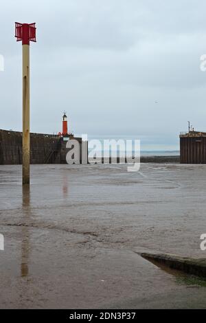 Vue depuis la rampe d'accès pour bateaux à travers le port de Watchet, Somerset, Angleterre, Royaume-Uni à marée basse, montrant les brise-lames et le phare. Banque D'Images