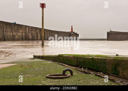 Vue depuis la rampe d'accès pour bateaux à travers le port de Watchet, Somerset, Angleterre, Royaume-Uni à marée basse, montrant les brise-lames et le phare. Banque D'Images