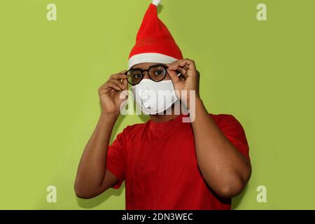 Noël pendant la pandémie du coronavirus COVID-19. Homme portant un masque chirurgical et un chapeau de père Noël. Modèle masculin portant des lunettes en costume de père noël. Banque D'Images