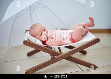 Le bébé repose sur une chaise longue sous un parapluie à la maison. Banque D'Images