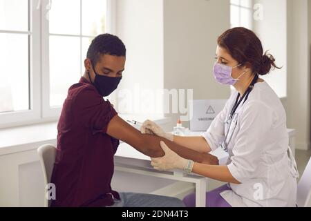 Femme médecin faisant la vaccination avec la seringue contre l'infection du coronavirus pour jeune homme noir Banque D'Images