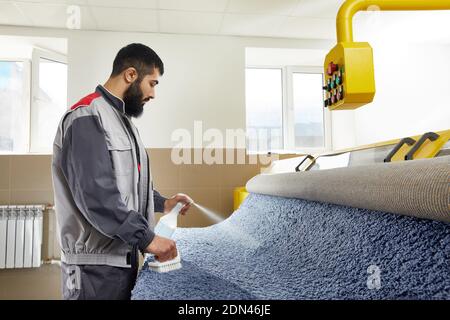 Homme portant un détergent de pulvérisation uniforme sur le tapis bleu à enlever Taches dans un service de nettoyage professionnel Banque D'Images