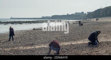 Personnes à la recherche de morceaux de verre de mer à utiliser comme décorations, ornements et bijoux de fantaisie parmi le sable et le shingle à Seaham dans le comté de Durham Banque D'Images