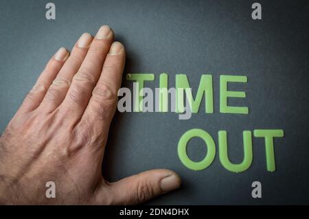 Main humaine à côté du mot Time Out écrit avec des lettres en plastique sur fond de papier gris foncé, concept Banque D'Images