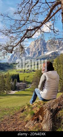 Une fille s'assoit sous un arbre et regarde les montagnes. Banque D'Images