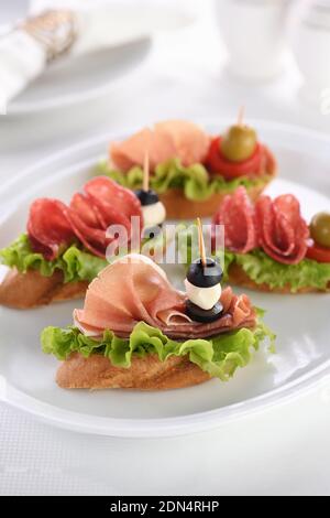 Canapés de baguette tendre avec laitue, salami ou jambon de Parme, tomates, mozzarella et olive. Plateau varié pour la fête. Banque D'Images