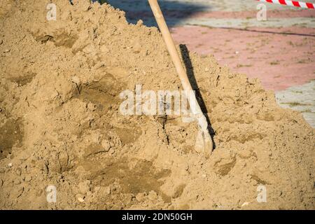 Une pile de sable avec une pelle coincée en elle sur un chantier de construction derrière une clôture Banque D'Images