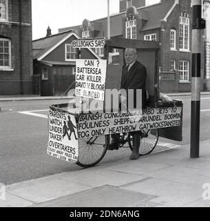 1960s, un militant historique, zélé et excentrique de la sécurité routière, l'ancien commandant de la marine Bill Boaks assis sur son célèbre vélo déocré avec des pancartes de protestation, à côté d'une route très fréquentée dans le sud de Londres, en Angleterre. ROYAUME-UNI. Le commandant Bill Boakes DSC héros naval et cycliste - une inspiration pour hurler Lord Sutch fondateur du parti officiel Monster Raving Loony - a tenu des élections parlementaires comme candidat pendant 30 ans tout d'abord sur un train, Bateaux et avions plate-forme et plus tard sur la sécurité routière campagne comme un monarchiste démocratique de sécurité publique blanc résident. Banque D'Images