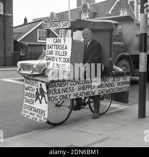 1960s, un militant historique, zélé et excentrique de la sécurité routière, l'ancien commandant de la marine Bill Boaks assis sur son célèbre vélo déocré avec des pancartes de protestation, à côté d'une route très fréquentée dans le sud de Londres, en Angleterre. ROYAUME-UNI. Le commandant Bill Boakes DSC héros naval et cycliste - une inspiration pour hurler Lord Sutch fondateur du parti officiel Monster Raving Loony - a tenu des élections parlementaires comme candidat pendant 30 ans tout d'abord sur un train, Bateaux et avions plate-forme et plus tard sur la sécurité routière campagne comme un monarchiste démocratique de sécurité publique blanc résident. Banque D'Images