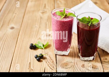 Boissons rafraîchissantes dans des verres en verre. Milk-Shake et smoothie. Baies de cassis et feuilles vertes sur fond de bois. Banque D'Images