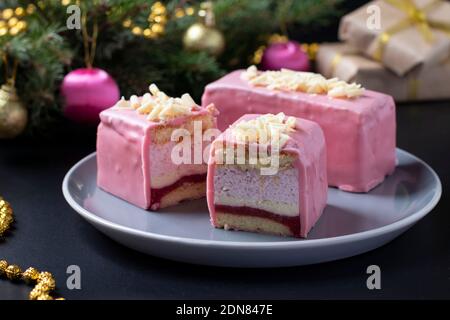 Desserts à la mousse en tranches avec biscuit aux amandes, coolie aux fraises et mousse aux fraises couverts de glaçage au chocolat rose gourmand sur fond de nouvel an. Banque D'Images