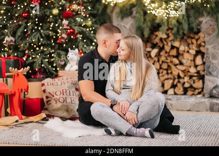 Adorable couple de mariage assis près de l'arbre de Noël et cheminée à la maison, le mari soin câlin belle femme enceinte, jeune famille profiter du bonheur, wint Banque D'Images