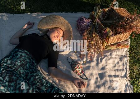 Femme se détendant pendant le verrouillage du coronavirus Colvid-19, dans le parc avec son masque facial recouvert d'un motif floral Banque D'Images