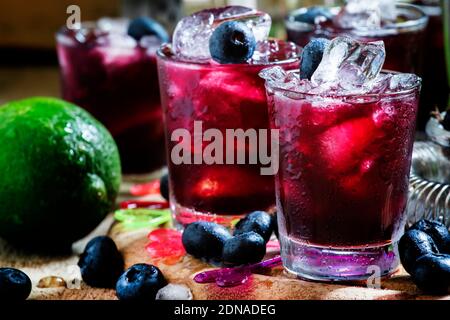 Cocktail alcoolique Darkside, avec liqueur, bleuet, jus de lime, glace pilée, outils de bar sur fond de bois vintage, concentration sélective Banque D'Images