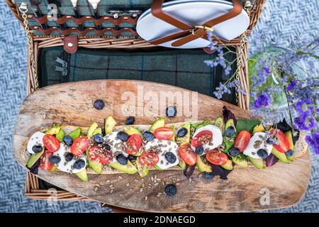 Plat de pique-nique d'été élégant, avec un panier pique-nique et une baguette végétarienne d'avocat, de tomates et de mozarella Banque D'Images