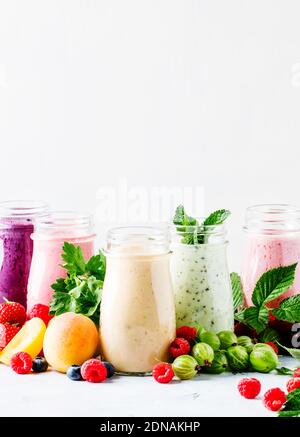 Smoothies aux baies colorées, sains et utiles, avec yaourt, fruits frais et baies sur fond gris, sélectif Banque D'Images