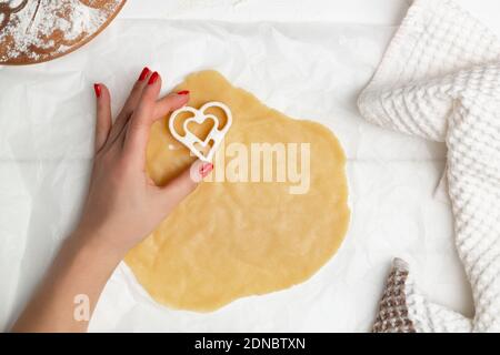 A woman's hand cuts heart-shaped cookies from rolled dough. Flat lay Stock Photo