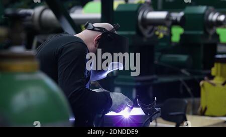 professional weld worker while using TIG Welding, wearing safety mask and protective clothing, selective focus background. Gas tungsten arc welding GT Stock Photo