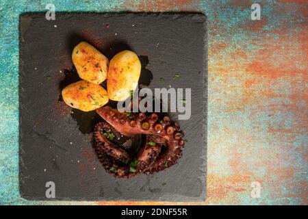 Grilled octopus tentacles with potatoes seasoned with Spanish paprika, olive oil, parsley and sea salt on a black slab and fancy background. Gourmet k Stock Photo