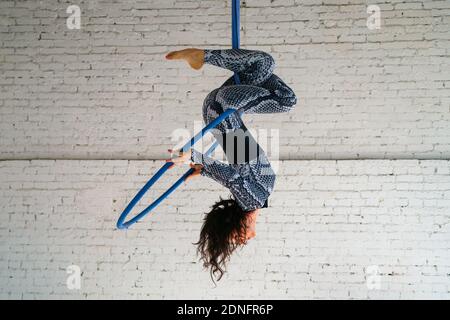 Une jeune brune est engagée dans des acrobaties aériennes dans une combinaison sur fond de brique blanche. Concept sportif. Équilibre. Banque D'Images