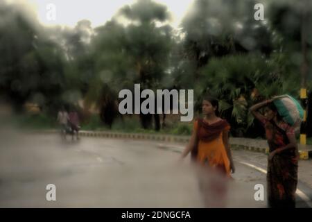 Les femmes en voyage, faisant un passage de route après une pluie en juillet, vu à travers un verre de fenêtre de voiture à Bihar, Inde. Banque D'Images