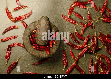 Indian stone Mortar and Pestle Set with Dried Red Chili in Mortar.Dried Red Chilis spread all over. Studio Shot Stock Photo