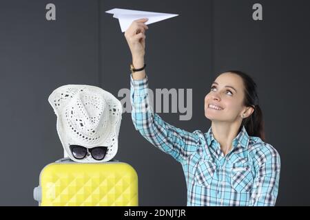 Femme avec valise jaune tenant un avion en papier