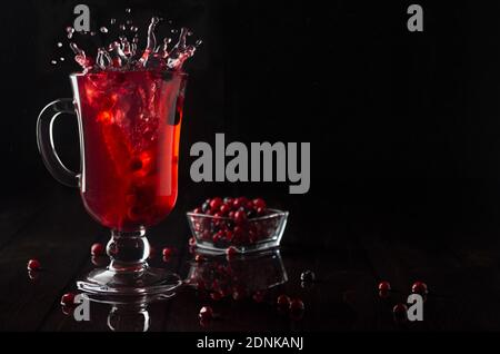 Thé aux baies rouges avec éclaboussures dans verre de vin avec baies mûres dans un intérieur noir élégant et sombre, espace de copie. Banque D'Images