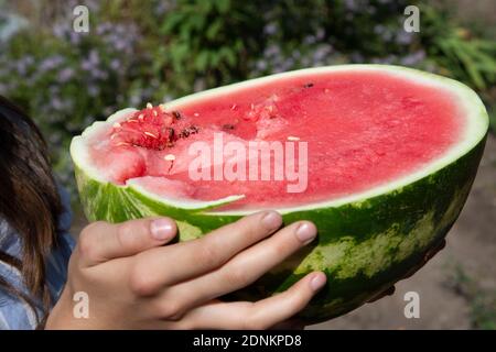 La moitié d'une grosse pastèque rouge juteuse dans les mains des enfants. Le concept de fruits vitaminés Banque D'Images