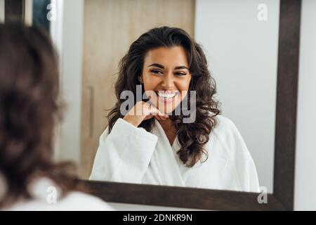Reflet de la femme heureuse dans le miroir portant un peignoir blanc Banque D'Images