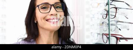 Femme avec des lunettes se tient à côté d'une vitrine avec optique. Banque D'Images