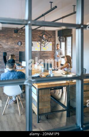 Jeune entraîneur donnant une discussion aux travailleurs dans un moderne bureau Banque D'Images