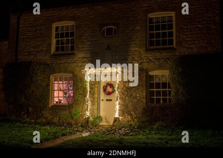 Cotswold cottage en pierre avec couronne de Noël et lumières la nuit. Guitting Power, Cotswolds, Gloucestershire, Angleterre Banque D'Images