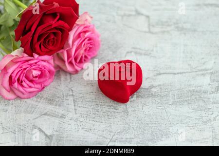 Boîte en velours rouge pour l'anneau d'engagement à côté d'un bouquet de roses avec espace pour le texte .cadeau romantique pour la Saint Valentin. Concept de proposition de mariage. Mise au point douce. Copier l'espace Banque D'Images