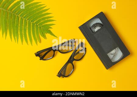 Lunettes 3D, cassette vidéo, fougères sur fond jaune. Vue de dessus, minimalisme Banque D'Images