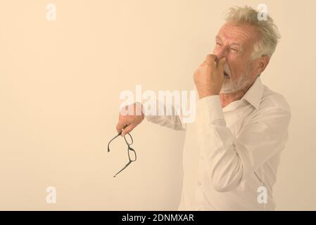 Studio shot of senior homme barbu couvrant le nez et à dégoûté tout en maintenant les lunettes contre fond blanc Banque D'Images