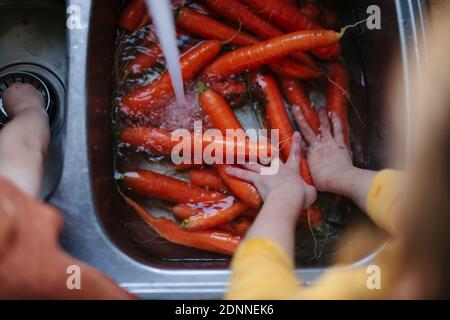 Une fille lavant des carottes dans un évier de cuisine Banque D'Images