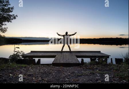 Walk in forest of Raismes-Saint Amand Wallers, Scarpe-Escaut Regional Nature Park (northern France). Man with arms outstretched at sunset on a pontoon Stock Photo
